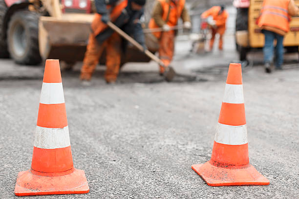 road workers repair the road,  cones in  foreground road workers repairing the road with shovels, dub asphalt with shovels at the back, the cones in the foreground urban road stock pictures, royalty-free photos & images