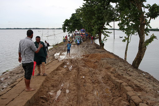 People walk on a flood-damaged road. As a result of climate change, people living in low-lying areas are often affected by floods due to heavy rains. Photo was taken from Sunamganj, Sylhet Division in Bangladesh on 6 July 2022.
