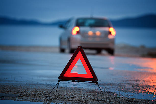 A roadside warning triangle and car with lights on wet road stock photo