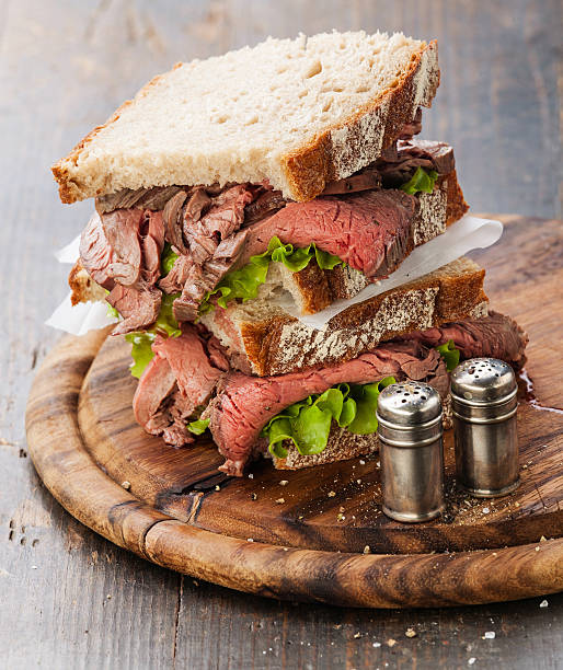 Roast beef sandwiches Roast beef sandwiches with lettuce on wooden cutting board on dark wooden background roast beef sandwich stock pictures, royalty-free photos & images