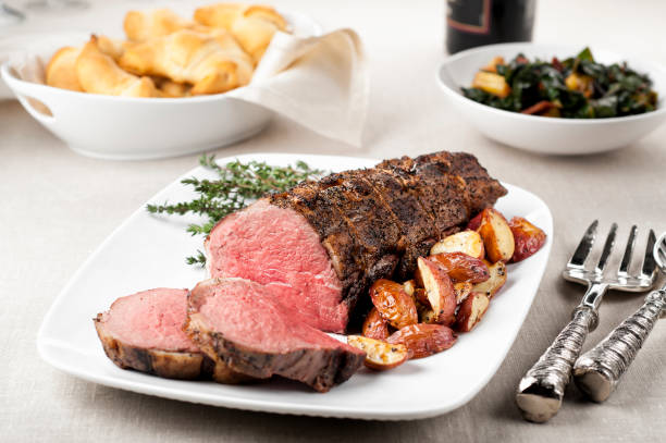 Roast beef tenderloin Roasted tenderloin of beef with roasted potatoes on a platter, sliced for serving. Rolls and green vegetable in background. roast dinner stock pictures, royalty-free photos & images