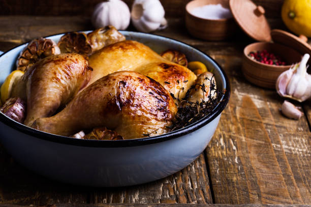 Roast chicken with garlic, thyme and lemon in cooking pan Roast chicken with garlic, thyme and lemon in cooking pan on rustic wooden background comfort food stock pictures, royalty-free photos & images
