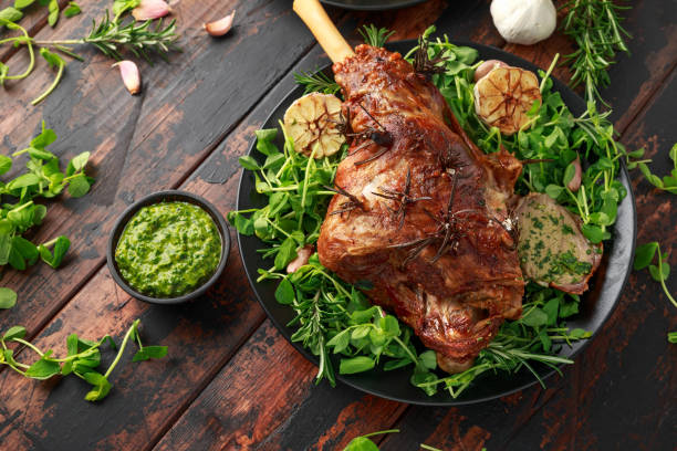 Roast Lamb leg with mint sauce, rosemary and garlic. on black plate, wooden table Roast Lamb leg with mint sauce, rosemary and garlic. on black plate, wooden table. mint leaf culinary stock pictures, royalty-free photos & images