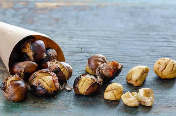 Roasted chestnuts Chestnuts in a paper cone on the wooden table chestnut food stock pictures, royalty-free photos & images