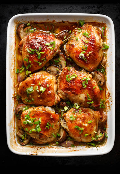 Roasted chicken thighs with mushrooms, garlic and herbs in a baking dish Roasted chicken thighs with mushrooms, garlic and herbs in a baking dish, top view chicken thigh meat stock pictures, royalty-free photos & images