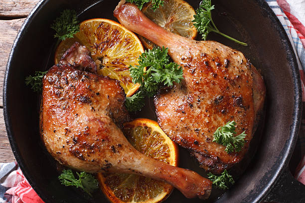 roasted duck legs in pan with oranges top view horizontal roasted duck leg with oranges in a pan close-up. horizontal view from above goose meat photos stock pictures, royalty-free photos & images