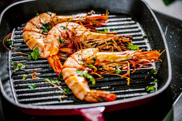 Roasted tiger prawns in iron grilling pan with  lemon, black background, top view stock photo