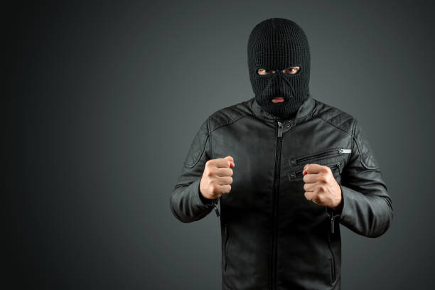 Robber, thug in a balaclava on a black background. Robbery, hacker, crime, theft. Copy space. Robber, thug in a balaclava on a black background. Robbery, hacker, crime, theft. Copy space ski mask criminal stock pictures, royalty-free photos & images