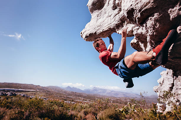 Rock climber bouldering outdoors on mountain in nature Rock climber holding on to rock overhang as he boulders up mountain. He is strong and focussed. rock face stock pictures, royalty-free photos & images