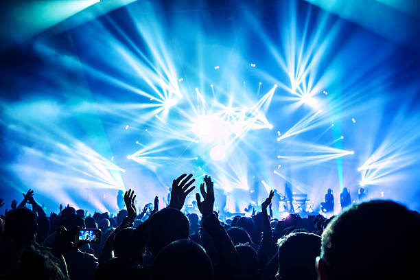 Rock concert Large group of happy people enjoying rock concert, clapping with raised up hands, blue lights from the stage, new year celebration concept rock musician stock pictures, royalty-free photos & images