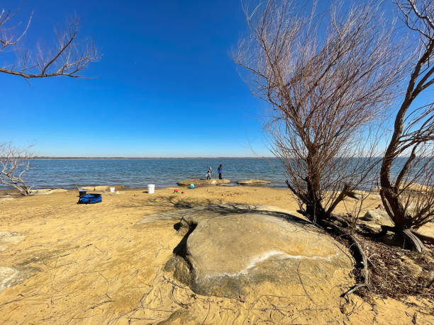 Rocky and sandy shoreline at Lake Lewisville, Texas, USA with unidentified kids playing in the distance stock photo