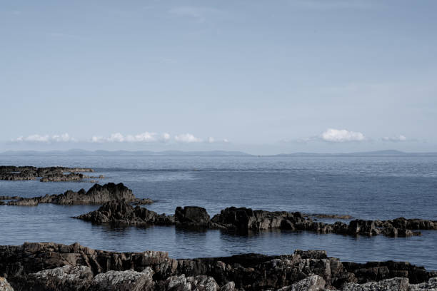 Rocky coastline, calm sea, blue sky and outline of island on horizon Rocky coastline of Strangford Penninsula near Ballyquintin, County Down (Northern Ireland),  a relatively calm Irish Sea, blue sky and the outline of the Isle of Man on the horizon. 

The rocky coastline is made up of interbedded greywacke sandstones and shales of turbiditic origin, which have been contorted through tectonic forces to steeply incline vertically. strangford lough stock pictures, royalty-free photos & images