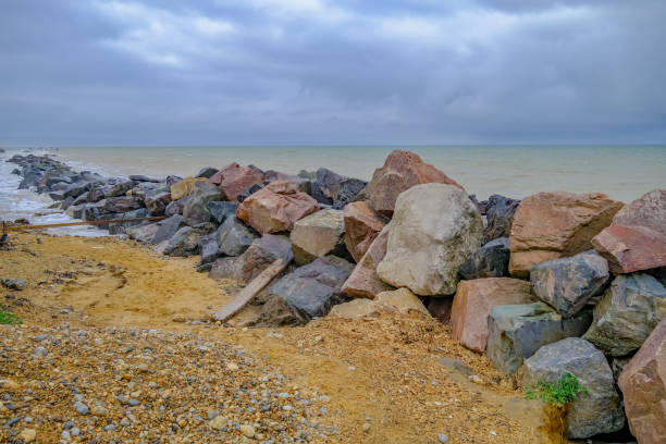 Rocky sea defences protecting against coastal erosion Pile of rocks serving as a barrier to protect the sandy cliffs from coastal erosion on Happisburgh beach on the Norfolk coast erosion control stock pictures, royalty-free photos & images