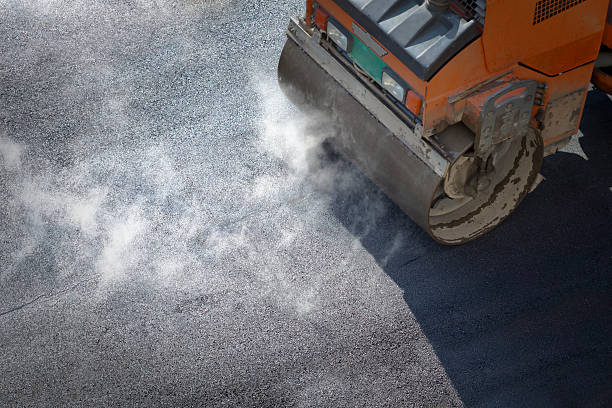 a roller compacting asphalt on a road - asfalt stockfoto's en -beelden