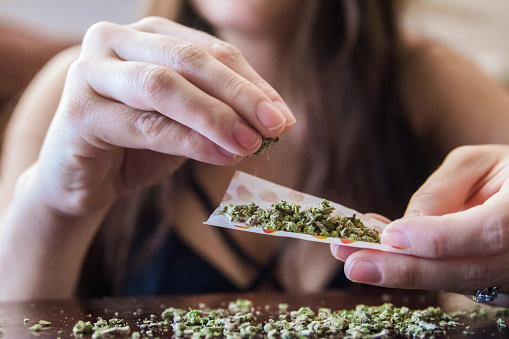 An anonymous woman placing marijuana flower into a joint paper to smoke.