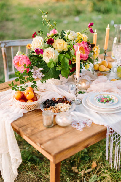romance, love, wedding, holidays, decoration, rest concept - romantic table setting with bright multicolored bouquet in centre, white feast serveware, slender candles and fruits and nuts stock photo