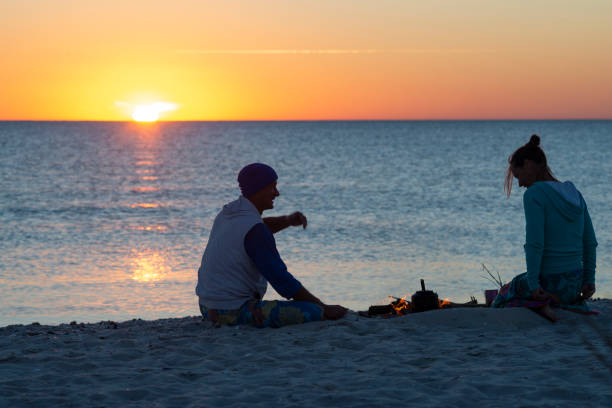 Romantic couple relaxes on a beach, making coffee on fire stock photo