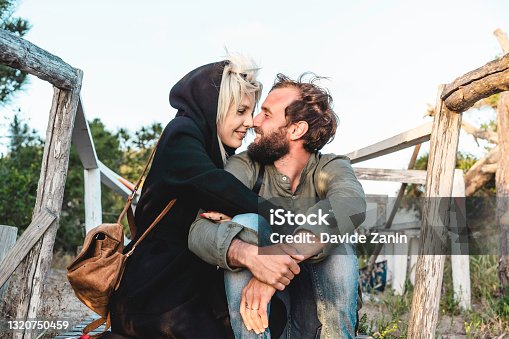 istock Romantic happy couple in love sitting on wooden stairs on dunes at the wild beach at sunset - Boyfriend and girlfriend looking into each other's eyes - Travellers in love - nature lovers concept 1320750459