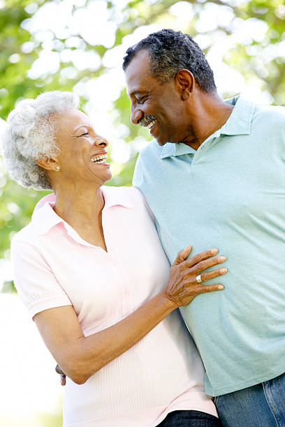 Romantic Senior African American Couple Walking In Park Romantic Senior African American Couple Walking In Park Smiling At Each Other old black couple in love stock pictures, royalty-free photos & images