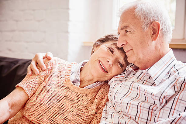 Romantic senior couple reminiscing on sofa Romantic senior couple sharing a moment remembering good times. They are sitting on a couch. nostalgia stock pictures, royalty-free photos & images
