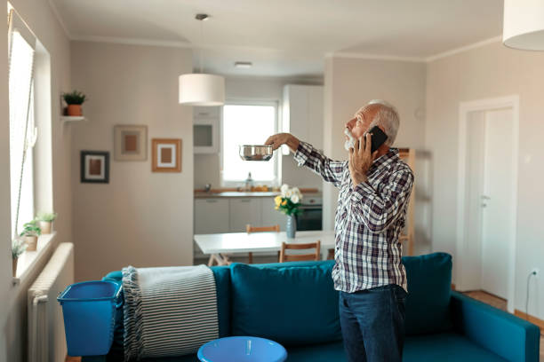 Roof Leaking Angry Bearded Senior Man Talking on Smartphone Near Plastic Wash Bowl at Home in the Living Room Because of Roof Leaking leaking stock pictures, royalty-free photos & images