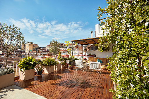 Spacious outdoor deck with hardwood floor, covered seating area, potted plants and a sun-filled view of the city.