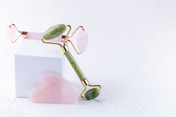 Rose quartz crystal and jade facial roller and massage tool Gua sha on white background, horizontal, copy space stock photo