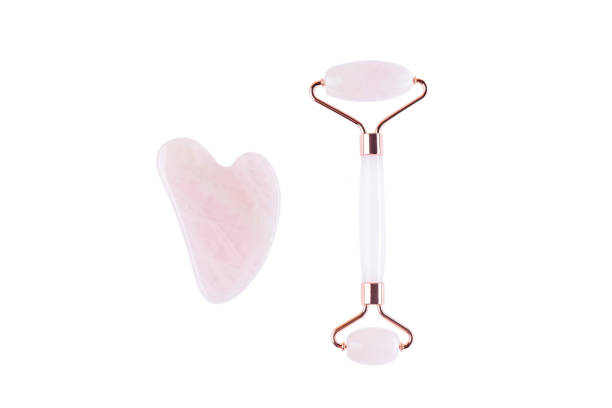 Rose quartz crystal facial roller and massage tool Gua sha isolated on white background stock photo
