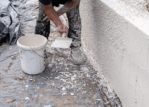 A skilled plasterer preparing to throw rough-cast harling mix onto the external wall of a residential home. The wet mortar and pebble mix is thrown at the plastered wall, creating an even layer of weatherproof wall protection, before it is left to dry before painting. It is hard work and requires accuracy to create a good and even covering around the whole house