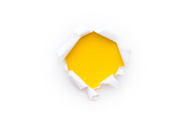 A round hole in white paper with torn edges isolated on a white background with a bright yellow color paper background inside. stock photo