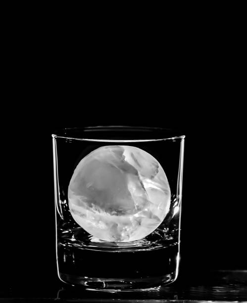 Round spherical ice cube ball in a cocktail glass with unique rim lighting against a black background. stock photo