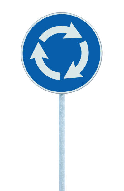 Roundabout crossroad traffic circle road sign isolated, blue, white arrows left hand drive direction, grey pole post, vertical closeup stock photo