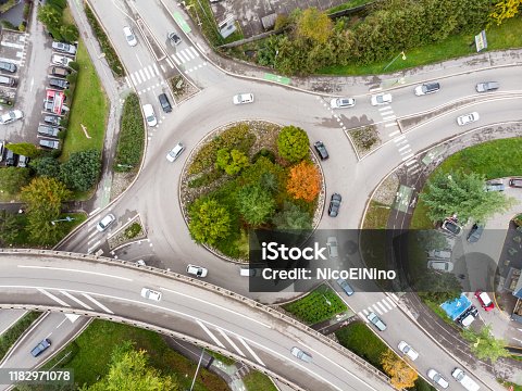 istock Roundabout road intersection with vehicle traffic and green trees aerial view from drone showing circular shape and lanes, transportation junction architecture 1182971078