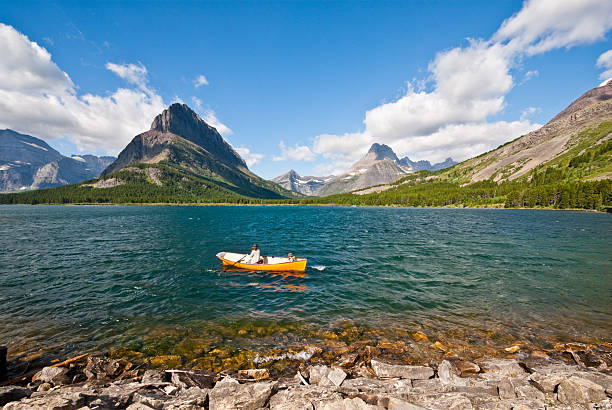 Rowing on Swiftcurrent Lake Glacier National Park, Montana, USA - August 17, 2013: A woman and young boy are rowing an orange boat on Swiftcurrent Lake on a windy day. jeff goulden glacier national park stock pictures, royalty-free photos & images