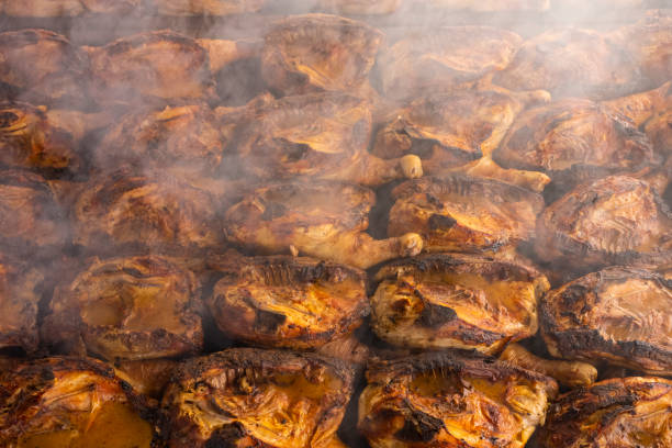 Rows of half chickens being roasted on a large barbecue grill  with smoke and the tasty scent of cooked chicken fills the air. stock photo