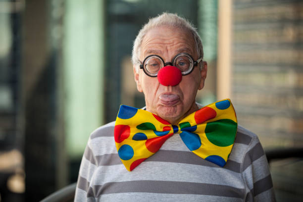 Rude Office Clown Senior man with glasses, bow tie and red nose, poking out his tongue. clown's nose stock pictures, royalty-free photos & images