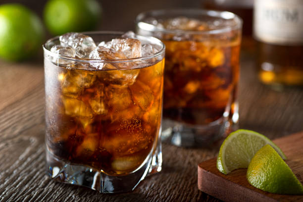 Rum and Cola Cuba Libre Rum and cola Cuba libre with lime and ice on a wooden bar top. rum stock pictures, royalty-free photos & images