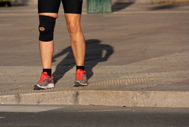 Runner woman that suffered a knee accident and now wears knee brace on the sidewalk stock photo
