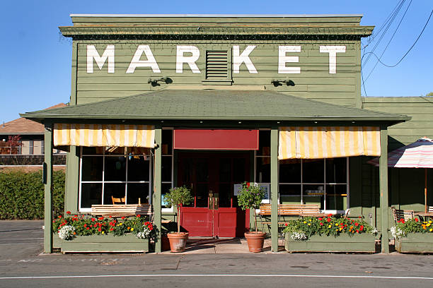 Rural Store Market Building in Country Small Town America Small town America, country market store and cafe in Yountville, Napa Valley, California, USA. Exterior of an old-fashioned rural retail shop building, painted green with yellow striped awnings and flower boxes, under a clear blue summer sky. small town america stock pictures, royalty-free photos & images