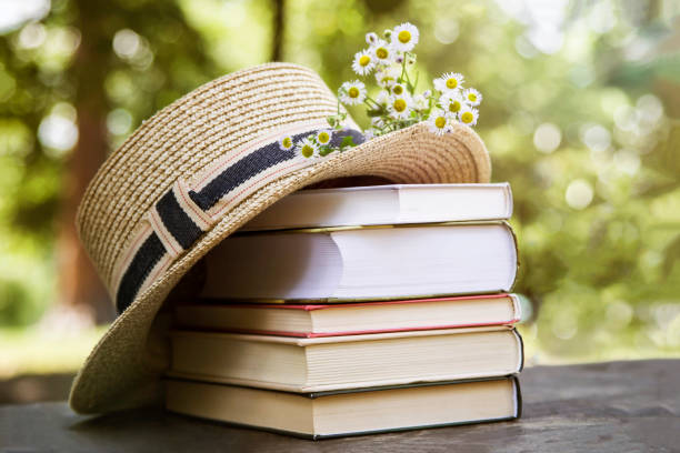 Rural summer still life in the park among trees. A stack of books on an old wooden table next to a straw hat of a canoe and a bouquet of wild flowers. blogging photos stock pictures, royalty-free photos & images