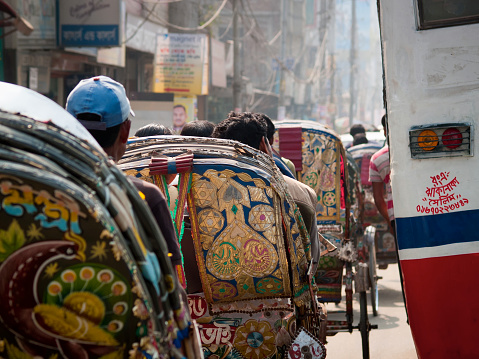 Dhaka, Bangladesh - January 23, 2012: Street full of colorful and brightly decorated rickshaws on the left side and a bus on the right, photographed from behind during rush hour in Dhaka city in Bangladesh.