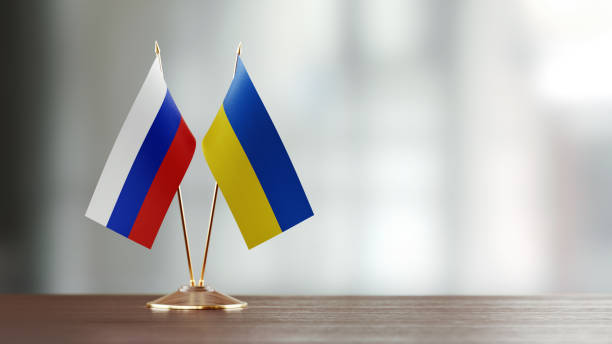 Russian and Ukrainian flag pair on desk over defocused background. Horizontal composition with copy space and selective focus.
