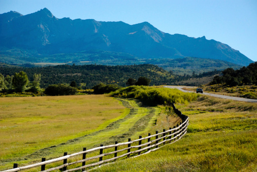Rustic fence and highway below Mount Sneffels near Ridgway Colorado showing pastures and beginnings of cutting hay.
