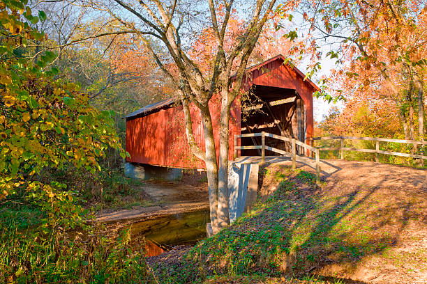 rustic red covered bridge - autumn red covered bridge across stream with early autumn color, in Missouri covered bridge stock pictures, royalty-free photos & images