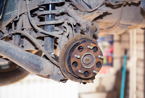Rusty hub and rear suspension on a raised vehicle. In the garage, a man changes parts on a vehicle. Small business concept, car repair and maintenance service. UHD 4K.