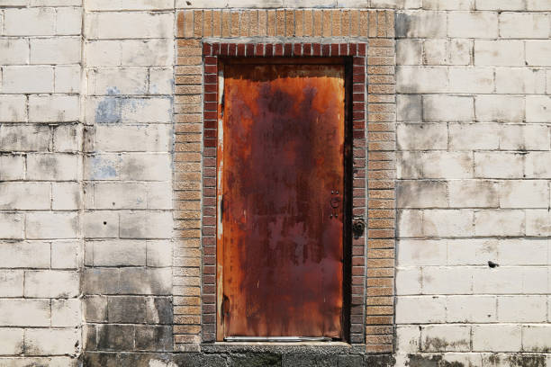 rusty red old metal steel door in a back alley concrete block abandoned warehouse building stock photo