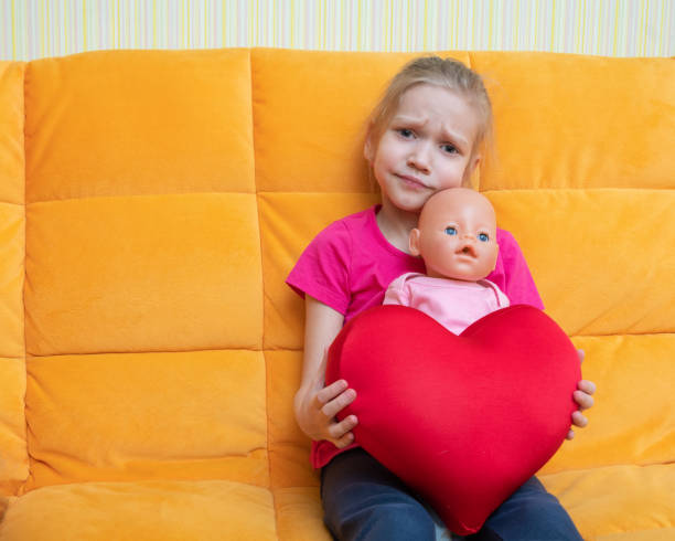 Sad adorable little girl holding a doll and a red heart pillow Sad adorable little girl holding a doll and a red heart pillow. broken doll 1 stock pictures, royalty-free photos & images