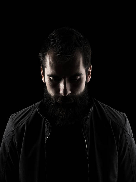 Sad bearded man looking down Sad bearded man looking down. High contrast low key dark shadow portrait isolated over black background. chiaroscuro stock pictures, royalty-free photos & images