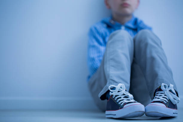 Sad boy sits alone Sad boy in sneakers with asperger's syndrome sits alone in his room childhood stock pictures, royalty-free photos & images