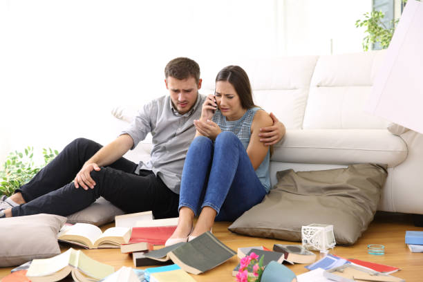 Sad couple calling to police after home robbery Sad couple calling to police sitting on the floor of the messy living room after home robbery burglary stock pictures, royalty-free photos & images